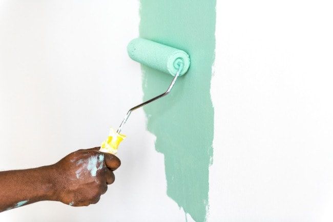 Painter rolling green paint onto an interior wall